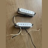 Dvě bílé snímače typu single-coil s pěti viditelnými póly. Snímače mají kovové montážní šrouby a jsou připojeny k černým a bílým vodičům. Na povrchu…
