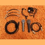 Sada vybavení složená ze dvou dynamických mikrofonů, kabelů a napájecího adaptéru. Na mikrofonech jsou viditelné nápisy "Sennheiser" a "Cobalt 810".…