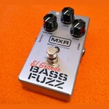 Stříbrný efekt pedál s třemi černými ovládacími knoflíky označenými jako VOLUME, TONE a FUZZ. Na horní části je logo MXR a nápis BASS INNOVATIONS, ve…