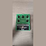 Zelený efekt pedál s černým panelem a bílými nápisy. Na černém panelu je velký nápis OVERDRIVE a logo Xvive. Na zelené části jsou čtyři černé ovládac…