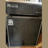 Černý basový zesilovač a reproduktorová skříň. Na horním přístroji je nápis Heritage SVT-CL, logo Ampeg a nápis Heritage. Spodní skříň má v horní čás…