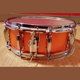 Pomalu vyfotocený oranžový snare drum s chromovaným obručováním a mechanismem. Na koruse nejsou viditelné žádné značky ani nápisy. Povrch nástroje vy…