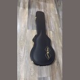 Černý tvrdý kufr na kytaru s zlatými zapojovacími prvky. Na povrchu je zlatý nápis Epiphone a logo Gibson Custom Shop v kosočtverci. Povrch kufru vyp…