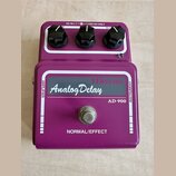 Fialový efekt pedál s nápisem Maxon Analog Delay a označením modelu AD-900. Na horní straně jsou tři černé oválné knoflíky a nápis DC IN.(-)—(+)DC12V…