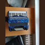 Modrá akordeon s povrchem v optice mramorování. Na přední straně je viditelné logo „Bacio“. Nástroj má bílé klávesy a bílá tlačítka basové strany. Po…