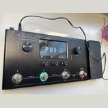 Černý efektový procesor s nápisem AMPERO Amp Modeler / Effects Processor. Zařízení má digitální displej, na kterém je zobrazen text P03-2 a další par…