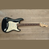 Černá elektrická kytara s bílým pickguardem a hnědým hmatníkem. Na hlavě je viditelné logo Fender a nápis STRATOCASTER. Kytara má tři snímače, pět úh…