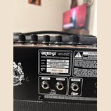 Detail zadní strany černého kytarového komba. Na štítku je uvedena značka ORANGE LONDON | ENGLAND VOICE OF THE WORLD, model CRUSH BASS 50, typ AMPLIF…