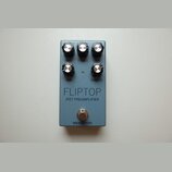 Modrý kytarový pedál s pěti černými ovládacími knoflíky. Na povrchu jsou nápisy BASS, TREBLE, GAIN, CAB a MASTER, dále velký text FLIPTOP a pod ním J…