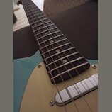 Detail elektrické kytary s modrým tělem a krčkem z tmavého dřeva. Kytara má světle béžový pickguard a chromovaný kryt snímače. Na hradenku jsou vidět…