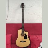 Akustická basová kytara s příměrem v těle, světlým topem a tmavými boky a hmatníkem. Na hlavě je viditelné logo Fender. Nástroj má černý plechtr ochr…