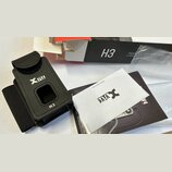 Černý kožený držák na vysílač s logem Xvive a označením H3. Vedle něj je položen bílý papír s logem Xvive a webovou adresou www.xvive.com, černý manu…