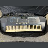 Černý digitální syntetizátor v černé přepravní brašně. Na přístroji je bílý nápis Roland E-56 SYNTHESIZER. Klávesnice vykazuje zežlutnutí bílých kláv…