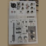 Bílá míchací konzole s nápisem YAMAHA a označením AG03 MIXING CONSOLE. Horní část obsahuje XLR vstup, dva jacky 6,35 mm s nápisy 2G GUITAR a LINE, or…