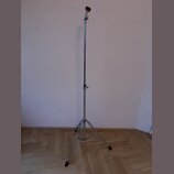 Stříbrný kovový mikrofonní stojan s tříramenným základnám a černými gumovými koncovkami nožiček. V horní části je umístěn držák s mikrofonem, který m…