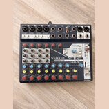 Černý mixážní pult s bílými a šedými popisky. Na předním panelu je vidět značka Soundcraft a název modelu NOTEPAD-12FX, dále nápis Lexicon EFFECTS a…
