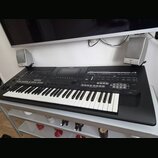 Černý digitální klavír s bílými a černými klávesami, umístěný na bílém stole. Na horním panelu jsou nápisy YAMAHA, 10th ANNIVERSARY a modelové označe…