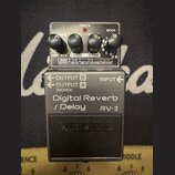 Šedý kytarový efekt s nápisem Digital Reverb / Delay RV-3 a logem BOSS na spínacím pedálu. Na horní části jsou čtyři černé otočné ovratky a přepínače…