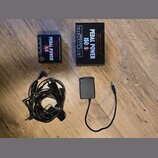 Na dřevěné podlaze jsou dvě černé napájecí zdroje pro efektové pedály a dva napájecí kabely. Menší zdroj má nápisy PEDAL POWER X4, ISOLATED DC OUTPUT…