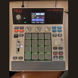 Bílá MPC Sample od značky AKAI professional. Zařízení má digitální displej, několik ovládacích knoflíků a 16 podsvícených padů s popisy funkcí. Na po…
