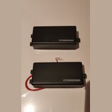 Dvě černé obdélníkové krabičky s nápisem STEINBERGER. Spodní kus má připojený červený kabel. Povrch je matný a v dobrém stavu.