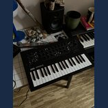 Černý syntetizátor s klaviaturou umístěný na podstavci. Na levé straně panelu je bílý nápis KORG minilogue xd a pod ním menší text POLYPHONIC HYBRID…
