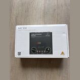 Fotografie znázorňuje bílý karton s produktem Behringer MIC300. Na krabici je nápis MIC300, Audiophile Vacuum Tube Preamplifier with Limiter a logo b…