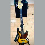 Elektrická basová kytara s korpusem v přechodovém žlutomodrém odstínu (sunburst) a tmavým hmatníkem. Na hlavě je viditelné logo "Fender". Kytara má č…
