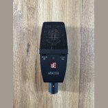 Černý dynamický mikrofon s kovovou mřížkou. Na těle jsou vidět přepínače s nápisy -10 0 -20 dB a 0 Hz, logo SE v červeném čtverci a modelové označení…