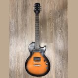 Elektrická kytara s tónem sunburst v oranžovo-černé kombinaci a tmavým hmatníkem. Na hlavě je bílý nápis Epiphone a pod ním stylizovaný nápis Les Pau…