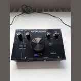 Černý audio rozhraní s nápisem M-AUDIO a označením modelu 192|4. Na předním panelu je velký centrální ovládací knoflík, čtyři menší knoflíky a logo a…
