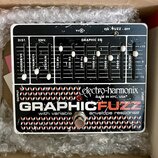 Kytarový efekt pedál v bílém rámu s černým ovládacím panelem. Na spodní části je nápis GRAPHIC FUZZ s přívlastkem with variable envelope response a l…