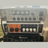 Fotografie zachycuje tři zesilovače naskládané na sebe. Horní je šedý s nápisy KATANA 500 BASS HEAD a BOSS POWER. Prostřední je bílý s oranžovým pane…