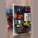 Sestava kytarových efektů v dřevěném rámu. Jsou zde pedály s nápisy ALPHA ONES, EVH 5150 overdrive, NUX ATLANTIS, ORANGE STAGE STAMP a BOSS NS-2 Nois…