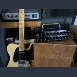 Na fotografii je elektrická kytara typu Telecaster v krémové barvě s černým pickguardem a javorovým hmatníkem. Vedle ní stojí černý kompaktní zesilov…