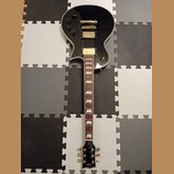 Černá elektrická kytara s tvarem single-cut a zlatým hardwarem. Na hlavě je bílý nápis "LTD". Hmatník má vložky ve tvaru trapézů. Povrch nástroje je…