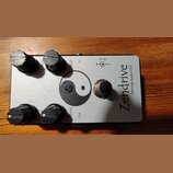 Stříbrný kytarový efekt s nápisem Zendrive a menším textem Hermida Audio USA. Na horní straně jsou čtyři černé otočné knoflíky s popisky Gain, Voice…