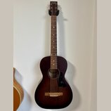 Akustická kytara s tmavě hnědým povrchem v přechodu (sunburst). Na hlavě hmatníku je bílý nápis „ArtLane“. Nástroj vykazuje čistý povrch bez viditeln…