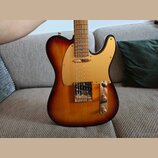 Elektrická kytara s tělem v provedení sunburst a zlatým pickguardem. Nástroj má jeden hmyzubový snímač u mostu a ovládací prvky v kovovém rámečku. Na…
