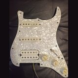Bílý pickguard s perleťovým efektem osazený třemi snímači. Na dvou horních snímačích je nápis „R.M. pickups“, na spodním humbuckeru je částečně vidit…