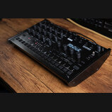 Černý digitální bubnový stroj s nápisy KORG a drumlogue HYBRID DRUM MACHINE. Zařízení obsahuje množství ovládacích knoflíků, malý displej s textem a…