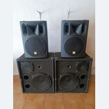 Dva černé reproduktorové boxy umístěné na dvou větších černých basových reproboxech s texturovaným povrchem. Horní boxy mají v horní části rohové mem…