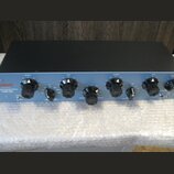 Modrý rackový procesor s černým horním krytem a řadou ovládacích knoflíků. V levém horním rohu je červené logo "Warm Audio" a nápis "TUBE EQ". Na pan…