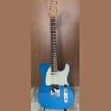 Modrá elektrická kytara typu Telecaster s bílým pickguardem a hnědým hmatníkem. Na hlavě krku je viditelné logo Fender. Nástroj vykazuje známky běžné…