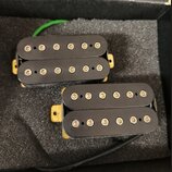 Dvě elektrické kytarové snímače typu humbucker s černými kryty. Snímače jsou umístěny na šedé pěnové výplasti v krabici. Na snímačích nejsou viditeln…