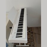 Bílé digitální piano na bílém stojanu s otevřeným krytem klávesnice. Na levé straně je nápis ES110 a na horní hraně těla nápis KAWAI. Nástroj vykazuj…