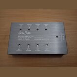 Stříbrný obdélníkový zdroj napájení z kovu s nápisy Harley Benton, PowerPlant ISO-1 Pro a ISOLATED OUTPUT POWER SUPPLY. Na horní straně jsou čtyři vý…