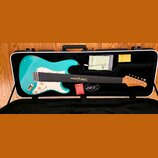 Tyrkysová elektrická kytara s bílým pickguardem v černém tvrdém kufru. Na hmatníku je nápis Xotic Guitars a na hlavě nástroje logo Xotic. V kufru se…