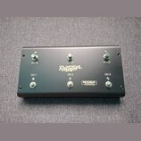 Černý obdélníkový spínací pedalboard s šesti kovovými přepínači. Na povrchu jsou bílé nápisy Rectifier., CH 1, CH 2, CH 3, MUTE, LOOP a SOLO. V dolní…