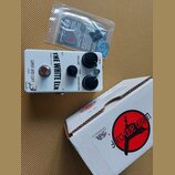 Bílý efekt pedál s nápisy THE WHITE ELK, SMALL FOOT a WREN and CUFF USA. Na horní straně jsou tři černé ovládací knoflíky s popisky VOLUME, TONE a DI…